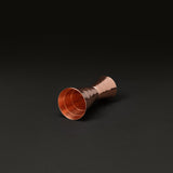 Solid copper cocktail jigger on its side, showing the hammered finish and the measuring line inside