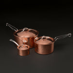 Three hammered copper saucepans with lids in graduated sizes