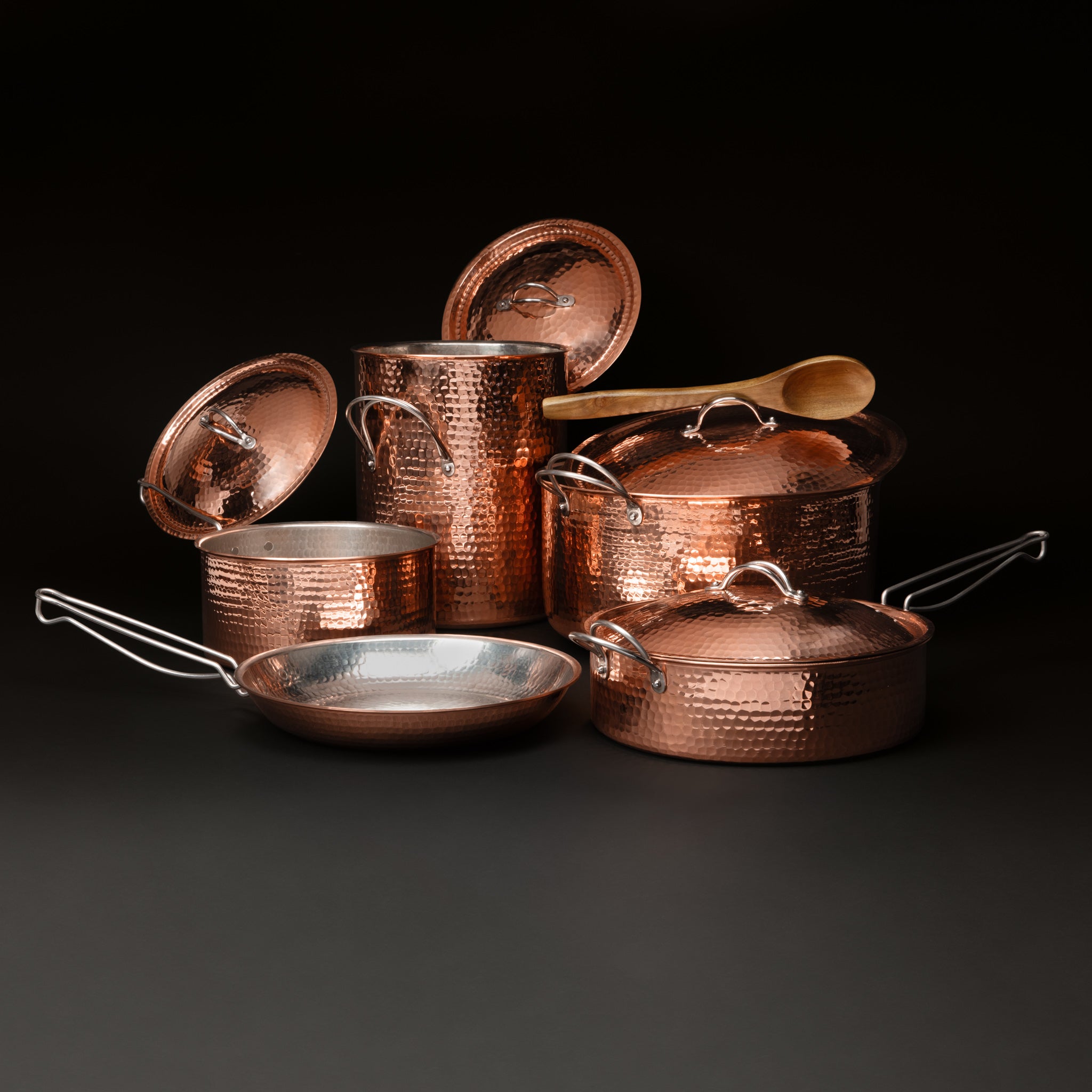 The stock pot, Dutch oven, and saucepan with lids lifted and a wooden spoon resting on the Dutch oven